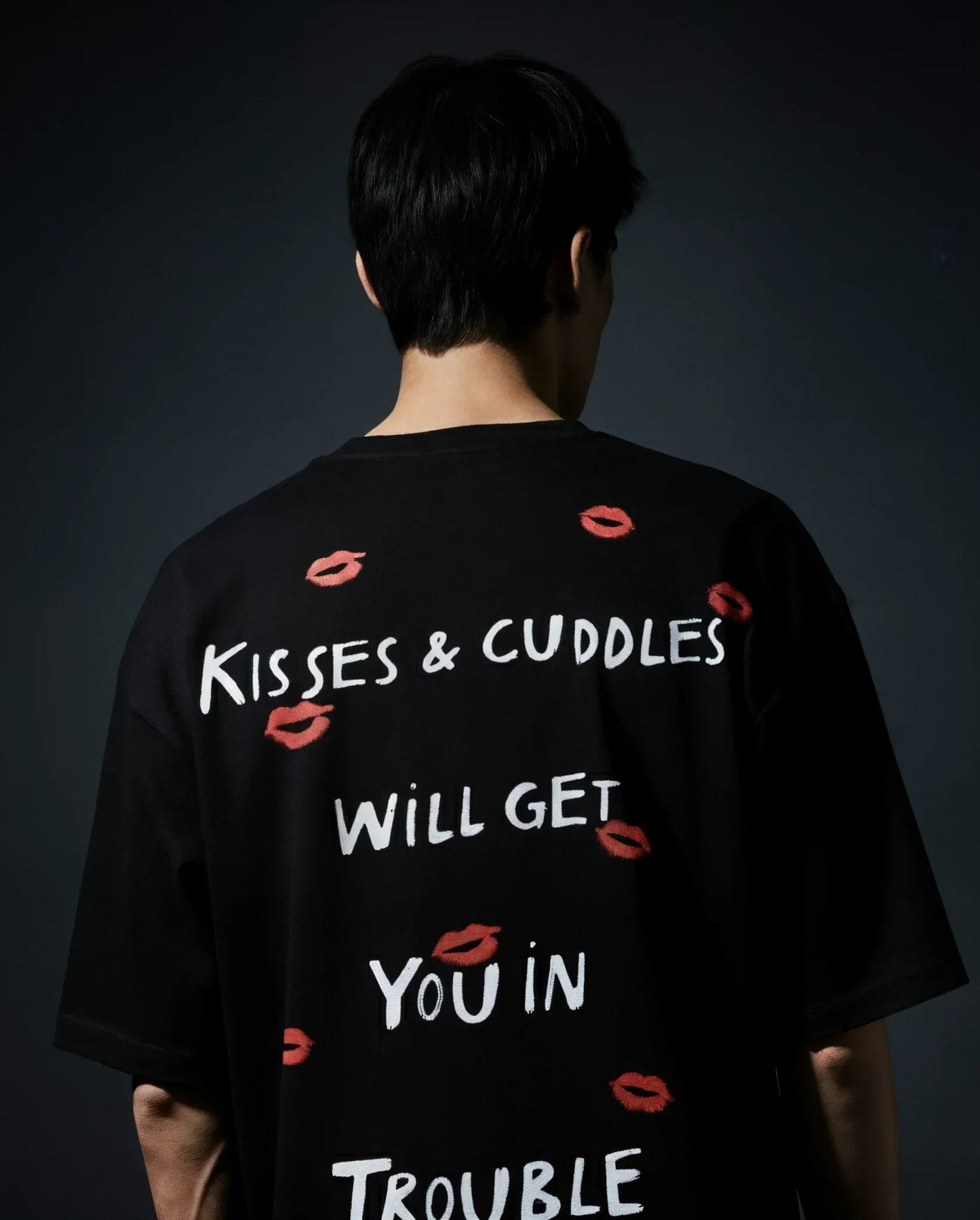 Person wearing a black t-shirt with text and red lip prints on a dark background