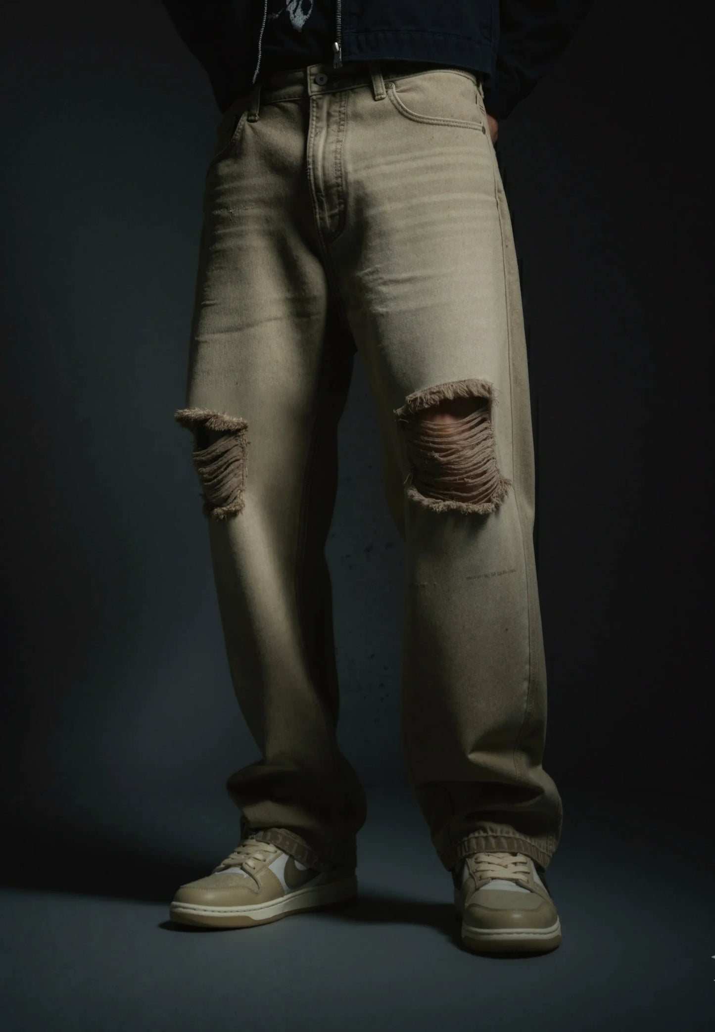 Ripped beige jeans worn by a person on a dark background