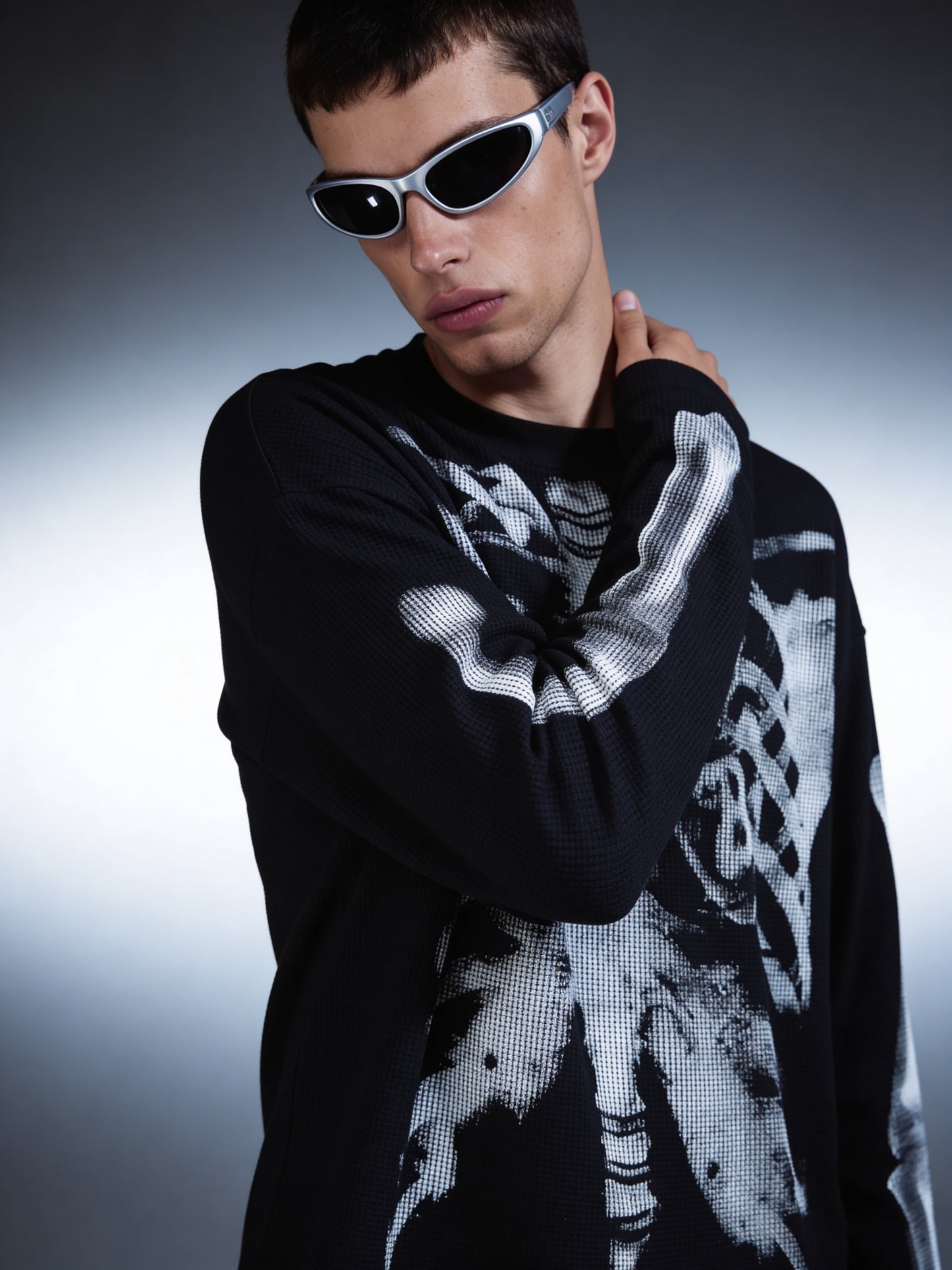 Person wearing a black and white patterned sweater with sunglasses on a gradient background