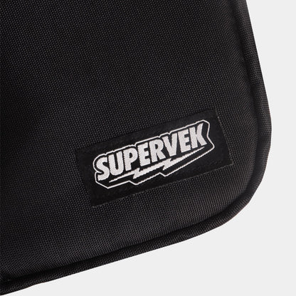 Detailed close-up of stitched Supervek logo patch on black "Sling" bag with textured fabric and Classic Black #color_Classic Black
