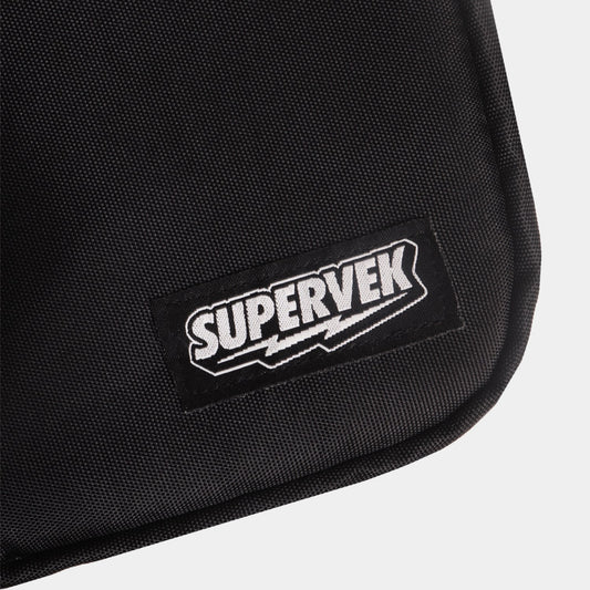 Detailed close-up of stitched Supervek logo patch on black "Sling" bag with textured fabric and Classic Black #color_Classic Black