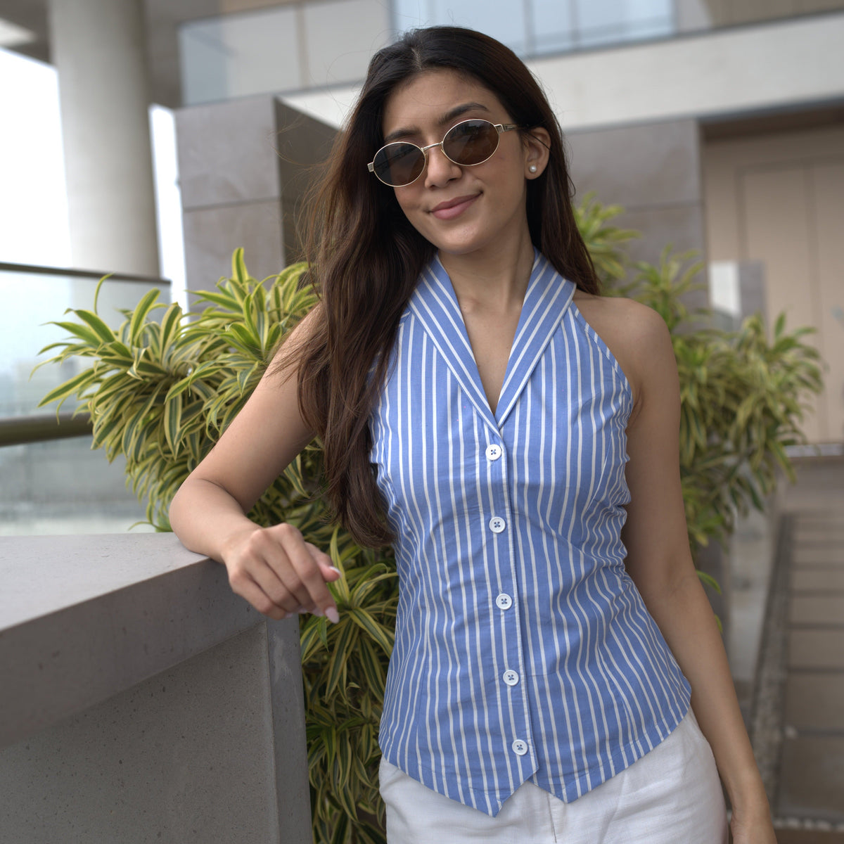 Woman in a blue and white striped shirt standing next to a plant indoors. Wearing Talia Vest and Goa Pants