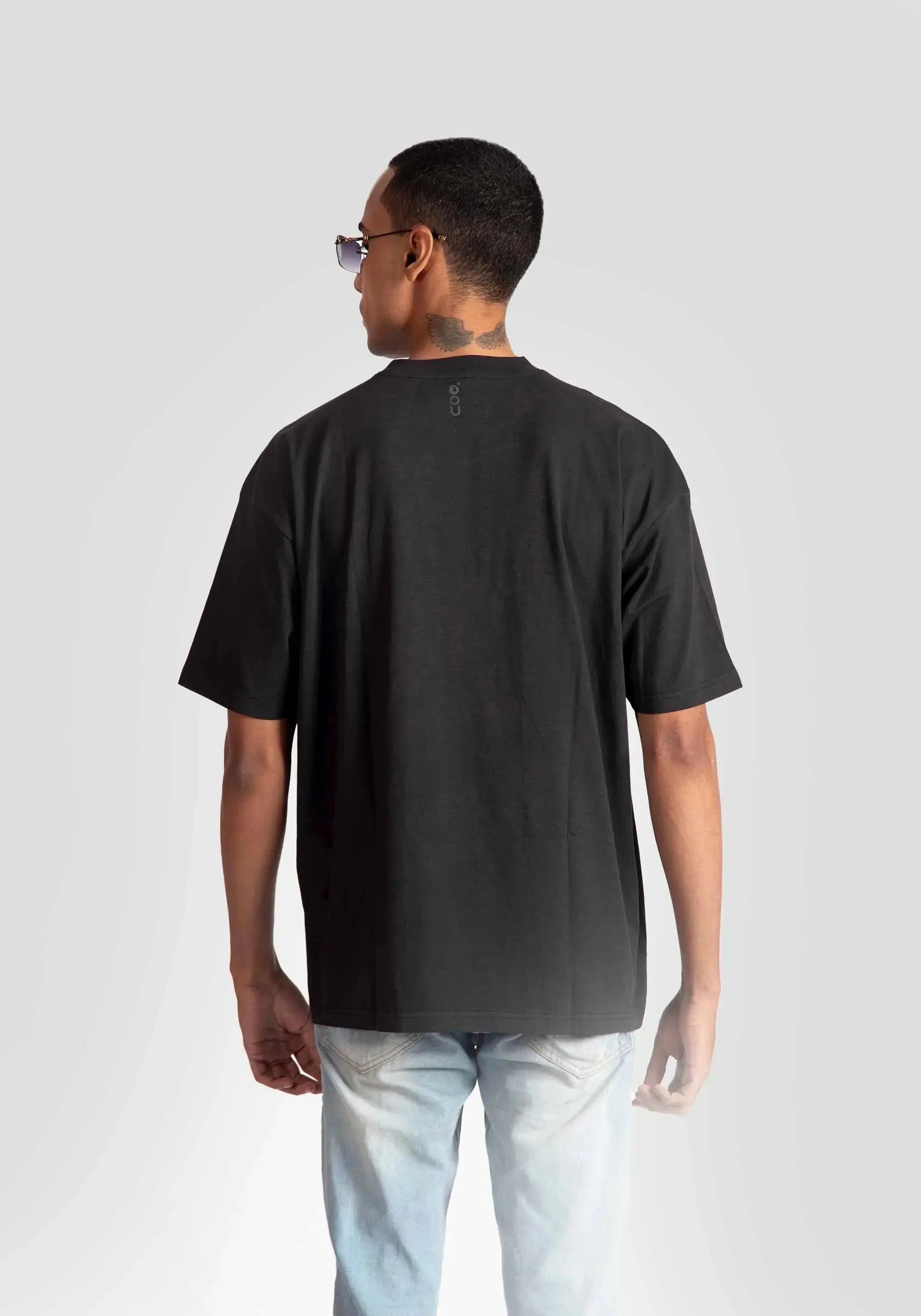 Back view of man wearing black oversized fashion t-shirt for men by Stylera with light wash jeans