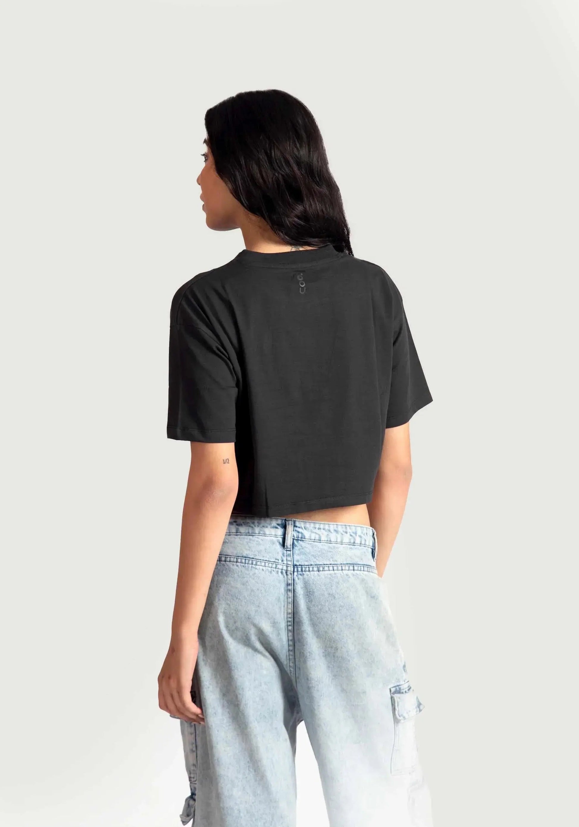 Back view of a woman wearing a trendy black oversized crop fit t-shirt paired with light blue jeans