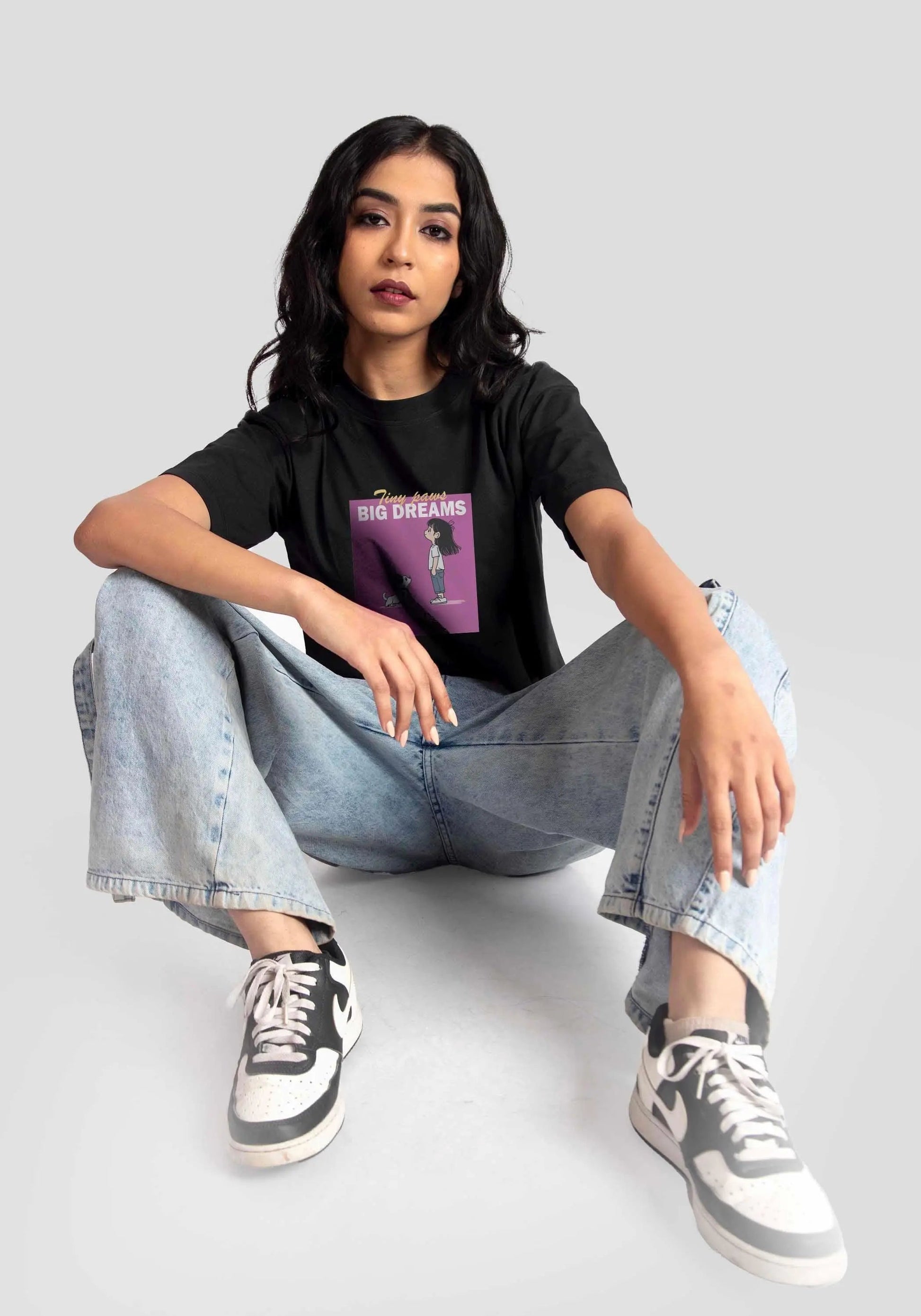Woman wearing a charcoal black oversized crop top with graphic print paired with light blue jeans and sneakers