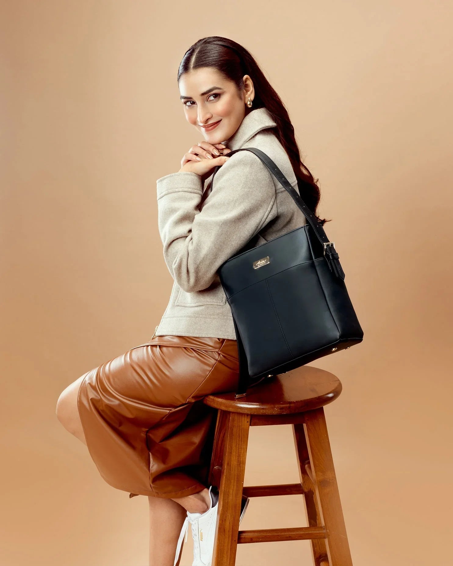 Fashion model showcasing charcoal chic bucket bag sitting on a stool in stylish attire