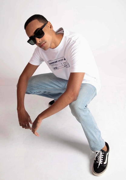 Man wearing Stylera white regular fit t-shirt with graphic print paired with light blue jeans and black sneakers