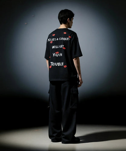 Person wearing a black t-shirt with text and red graphics on the back, standing against a dark background.