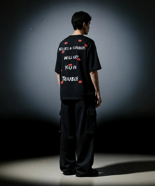 Person wearing a black t-shirt with text and red graphics on the back, standing against a dark background.