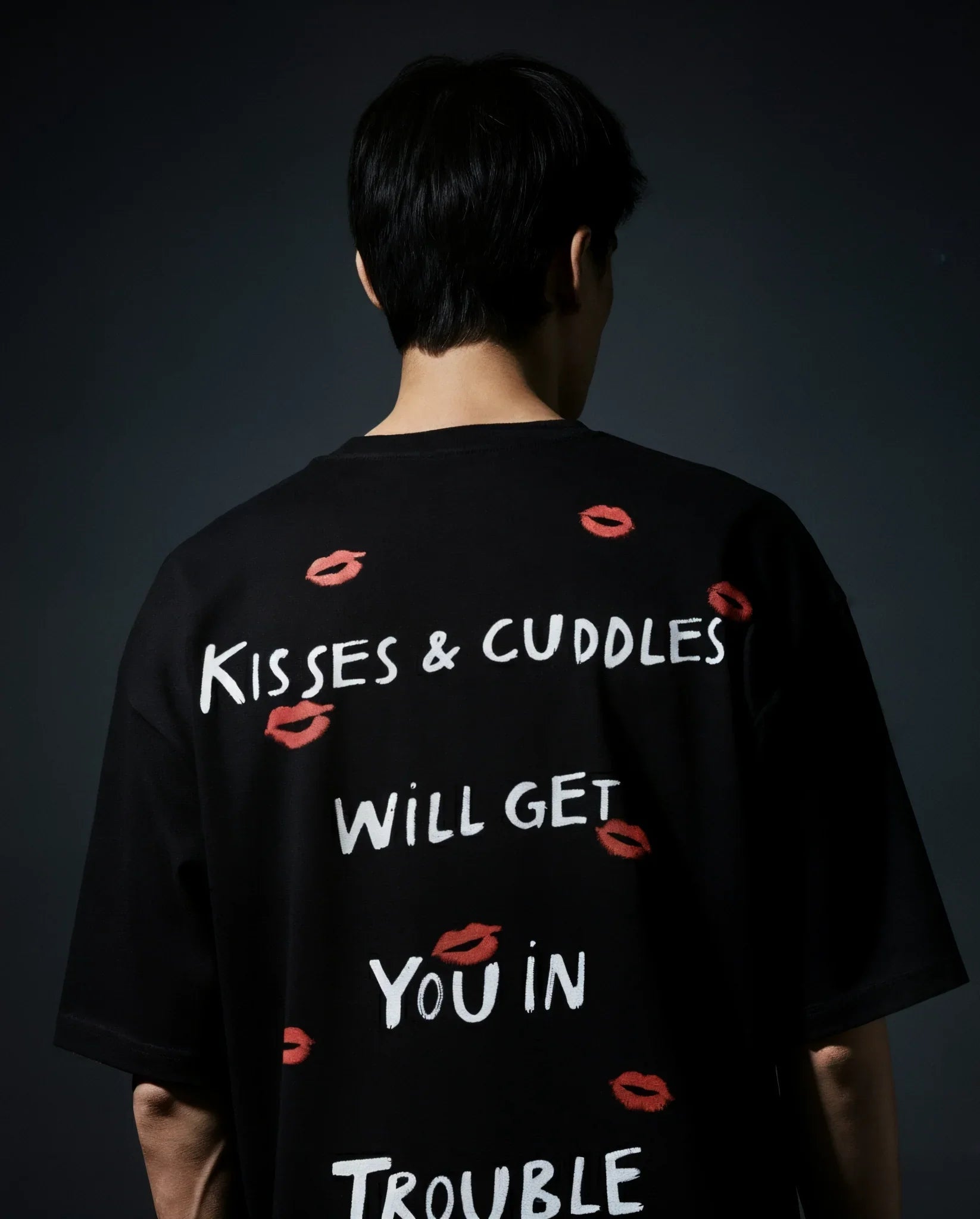 Person wearing a black t-shirt with text and red lip prints on a dark background