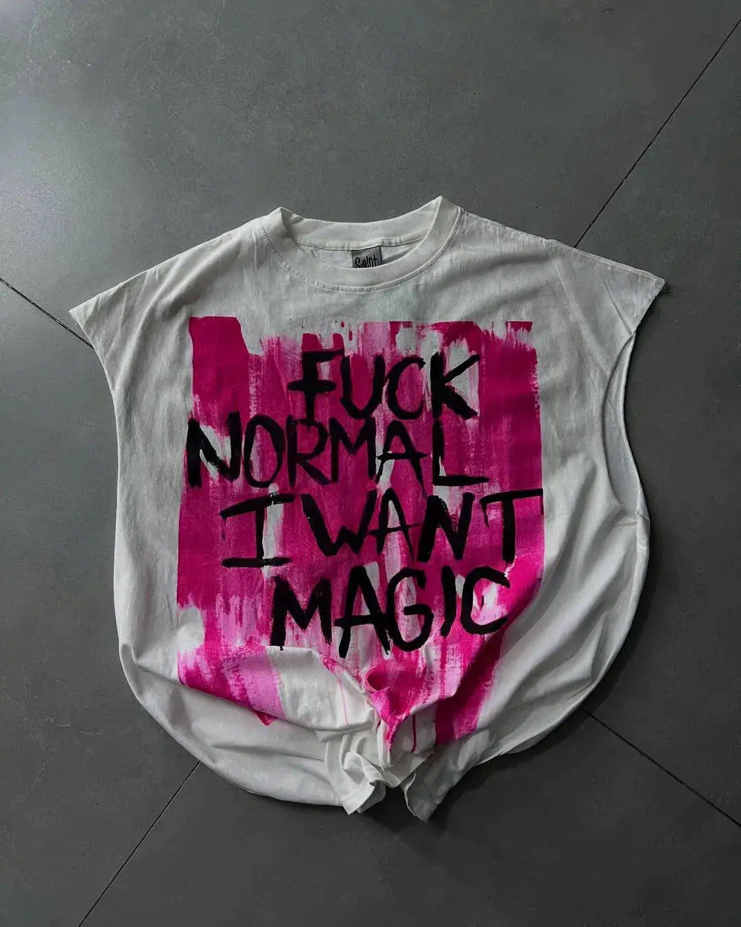 Gray t-shirt with pink and black text on a gray floor