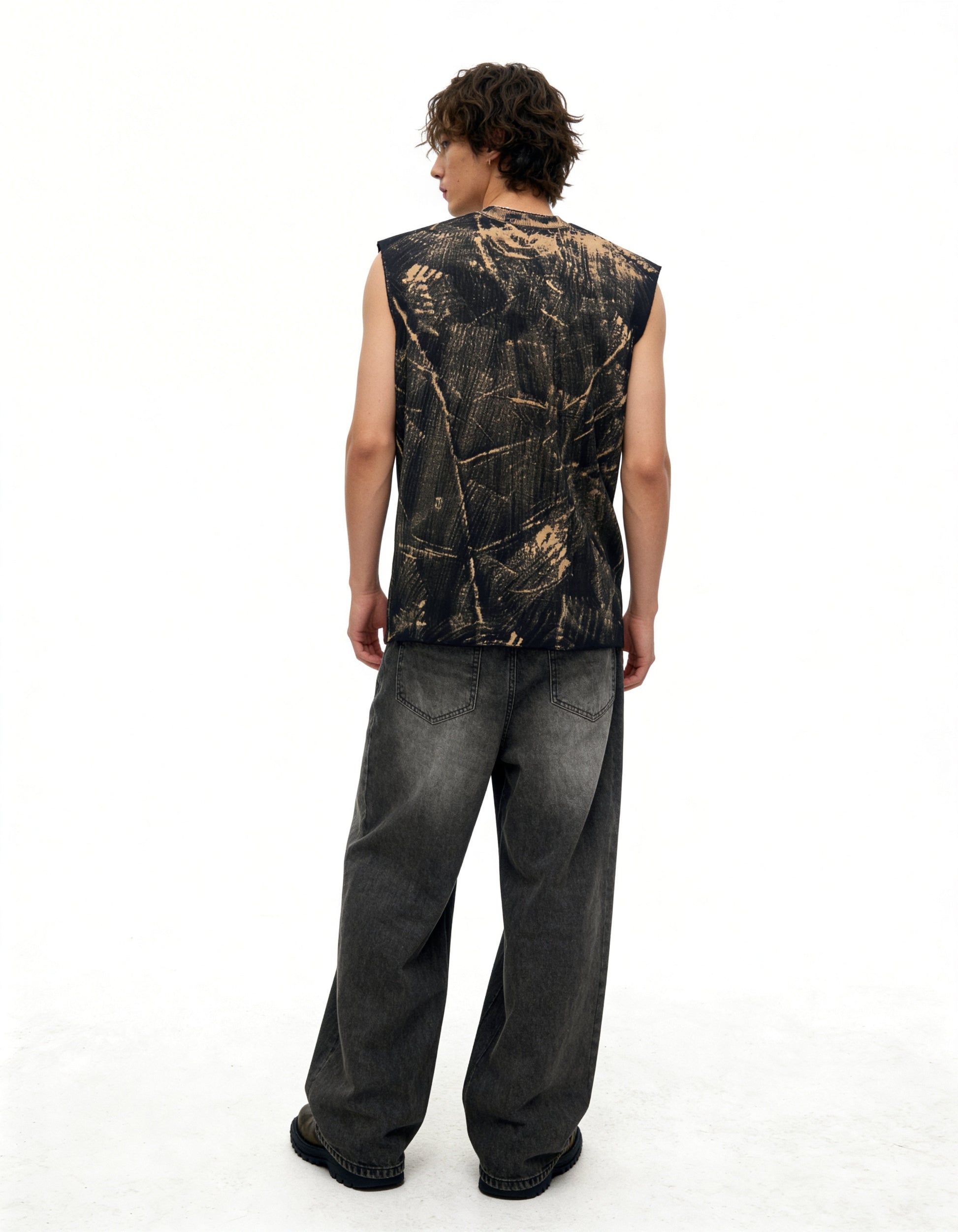 Person wearing a sleeveless camouflage shirt and dark jeans on a white background