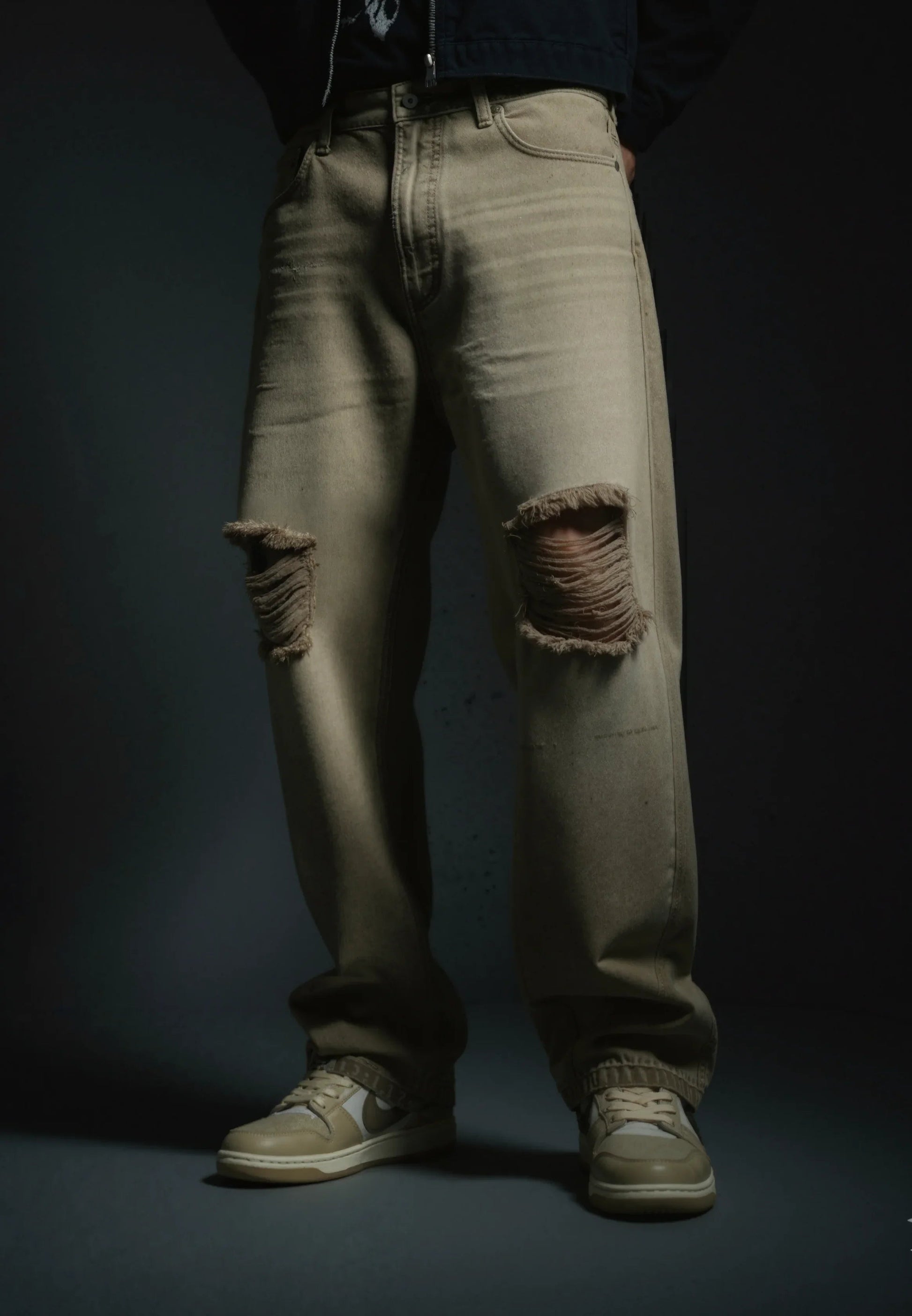 Ripped beige jeans worn by a person on a dark background