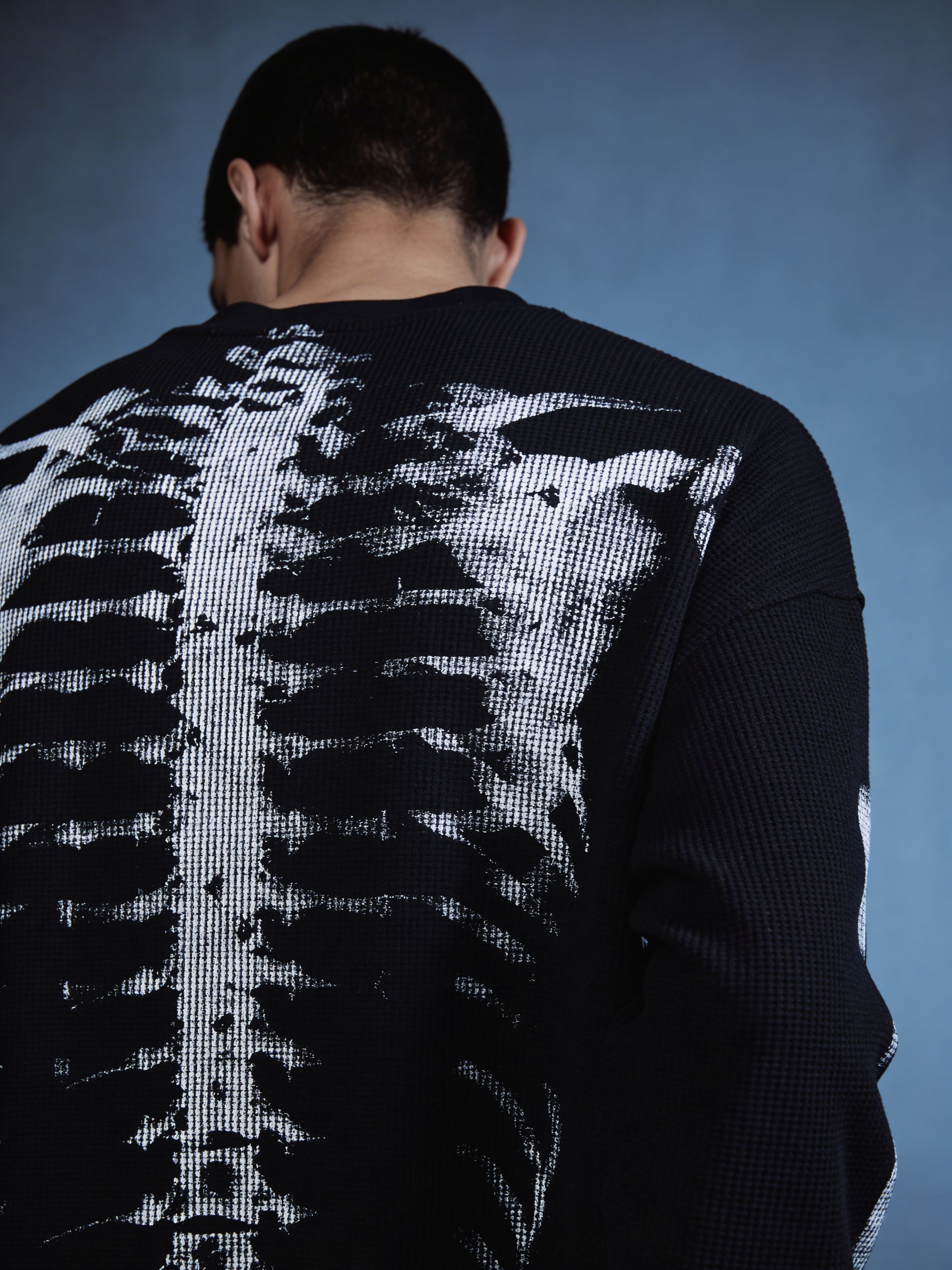 Person wearing a sweater with a skeleton design on the back against a blue background