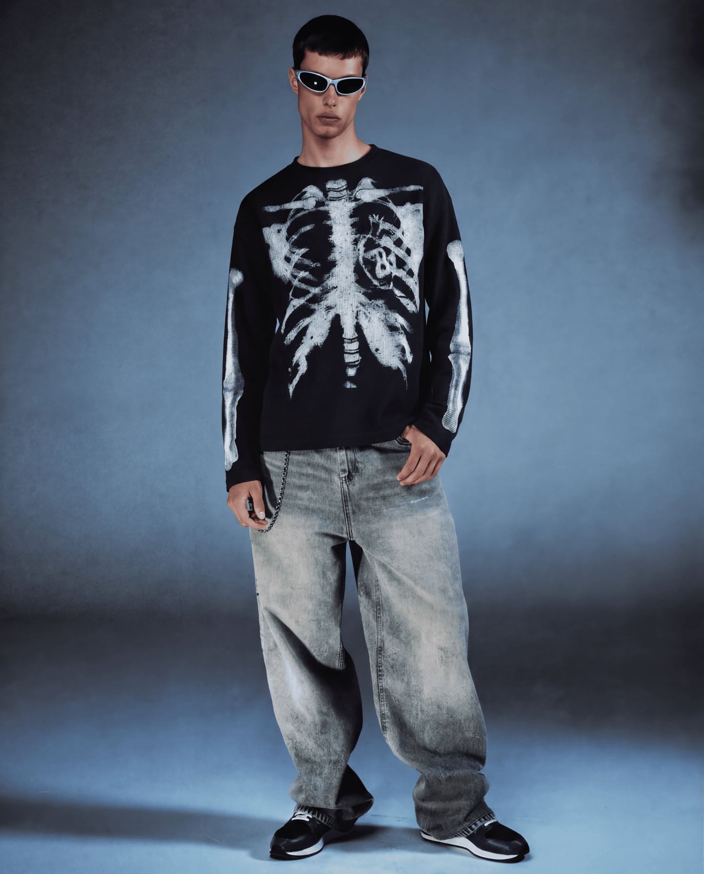 Person wearing a black sweater with a white skeleton design and light blue jeans against a gray background