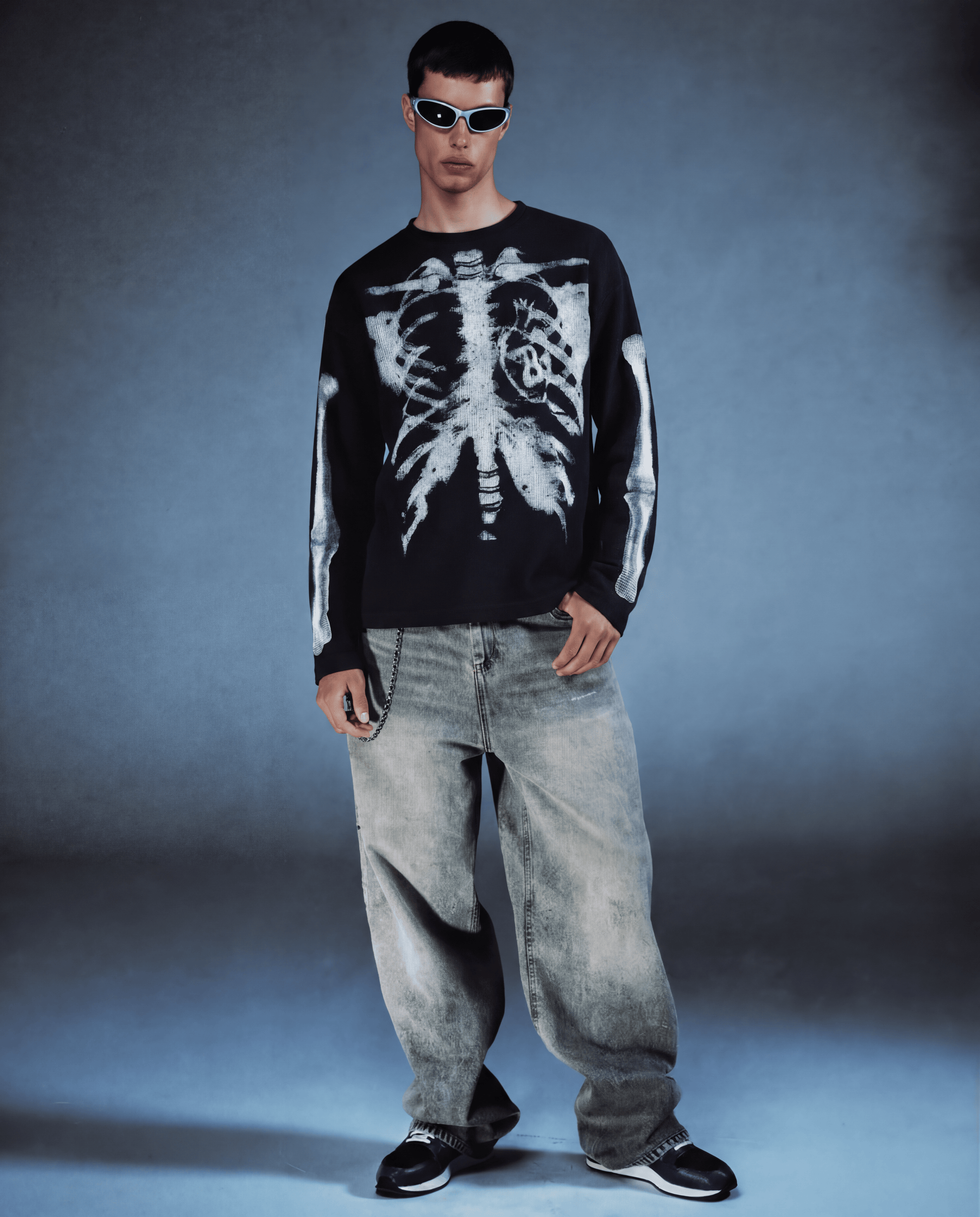 Person wearing a black sweater with a white skeleton design and light blue jeans against a gray background