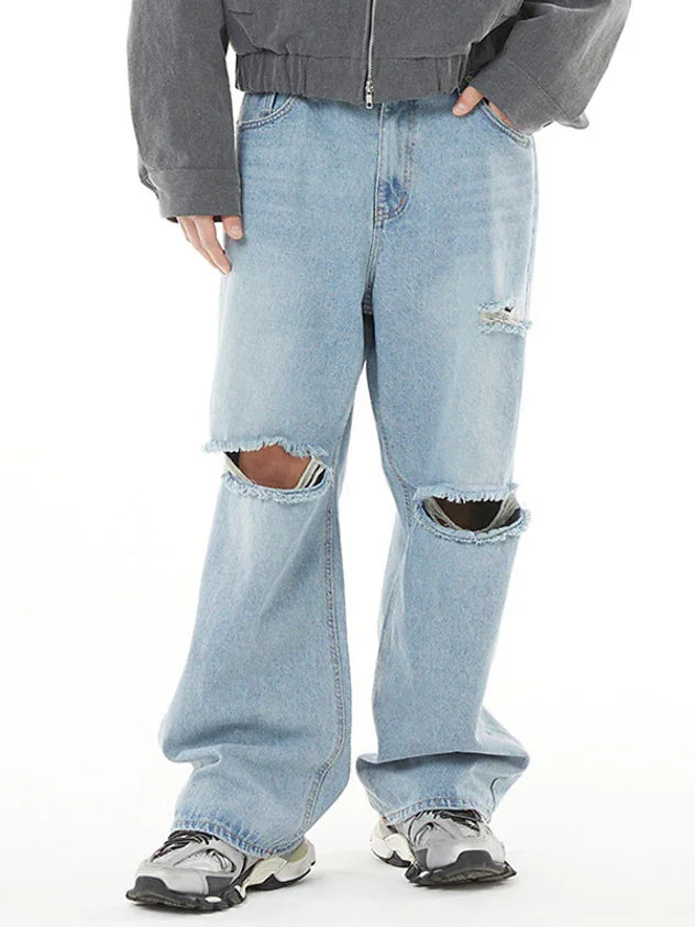 Front view of men wearing slash cut light blue baggy denim jeans with white sneakers.