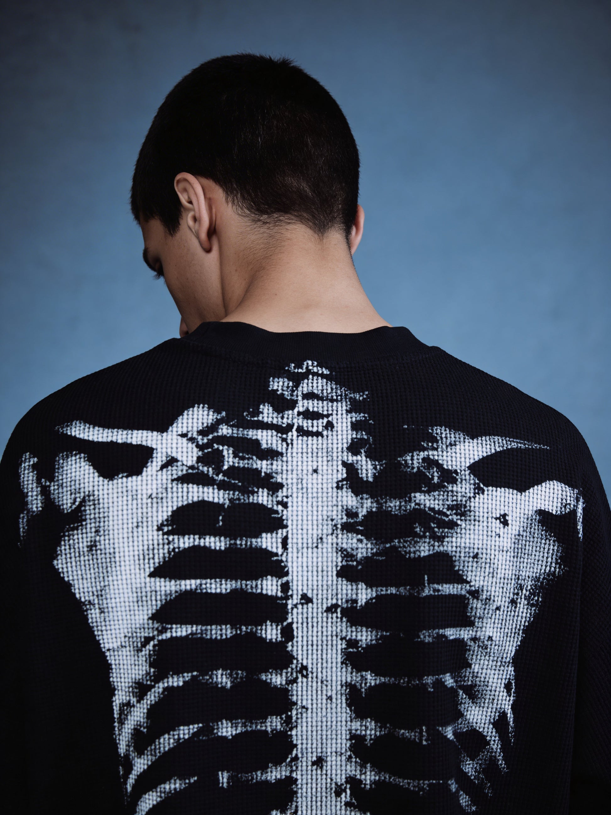 Person wearing a black sweater with a digital skeleton design on the back against a blue background