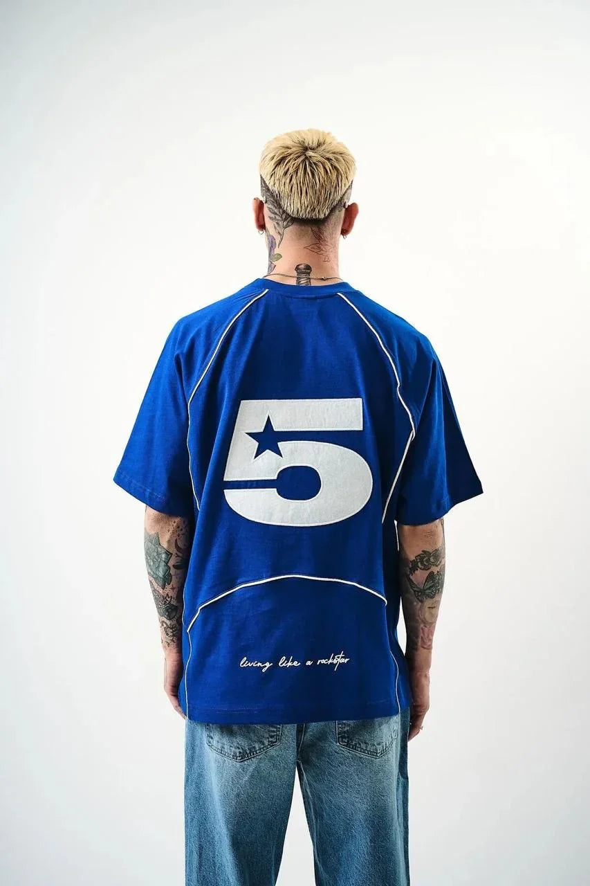 Person wearing a blue t-shirt with a large white number 5 on the back, standing against a white background.