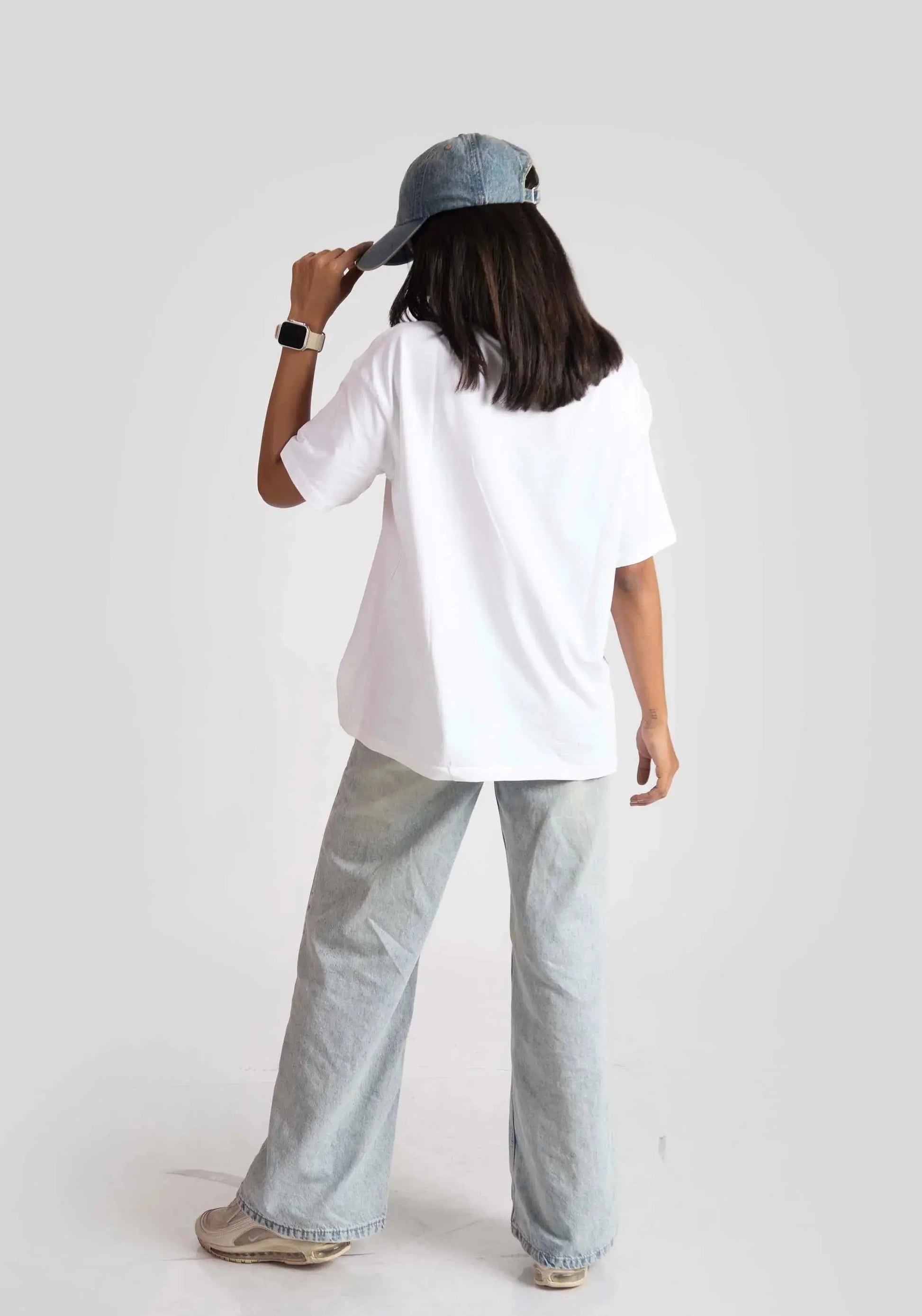 Woman wearing a white good vibes only graphic tee for women with light wash jeans and a blue cap