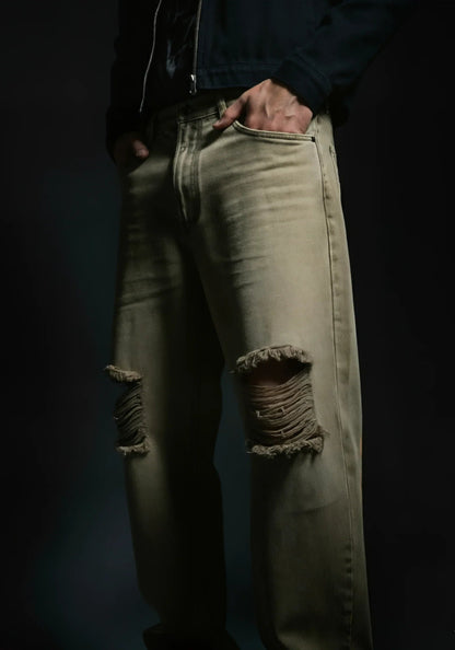 Person wearing distressed beige jeans against a dark background
