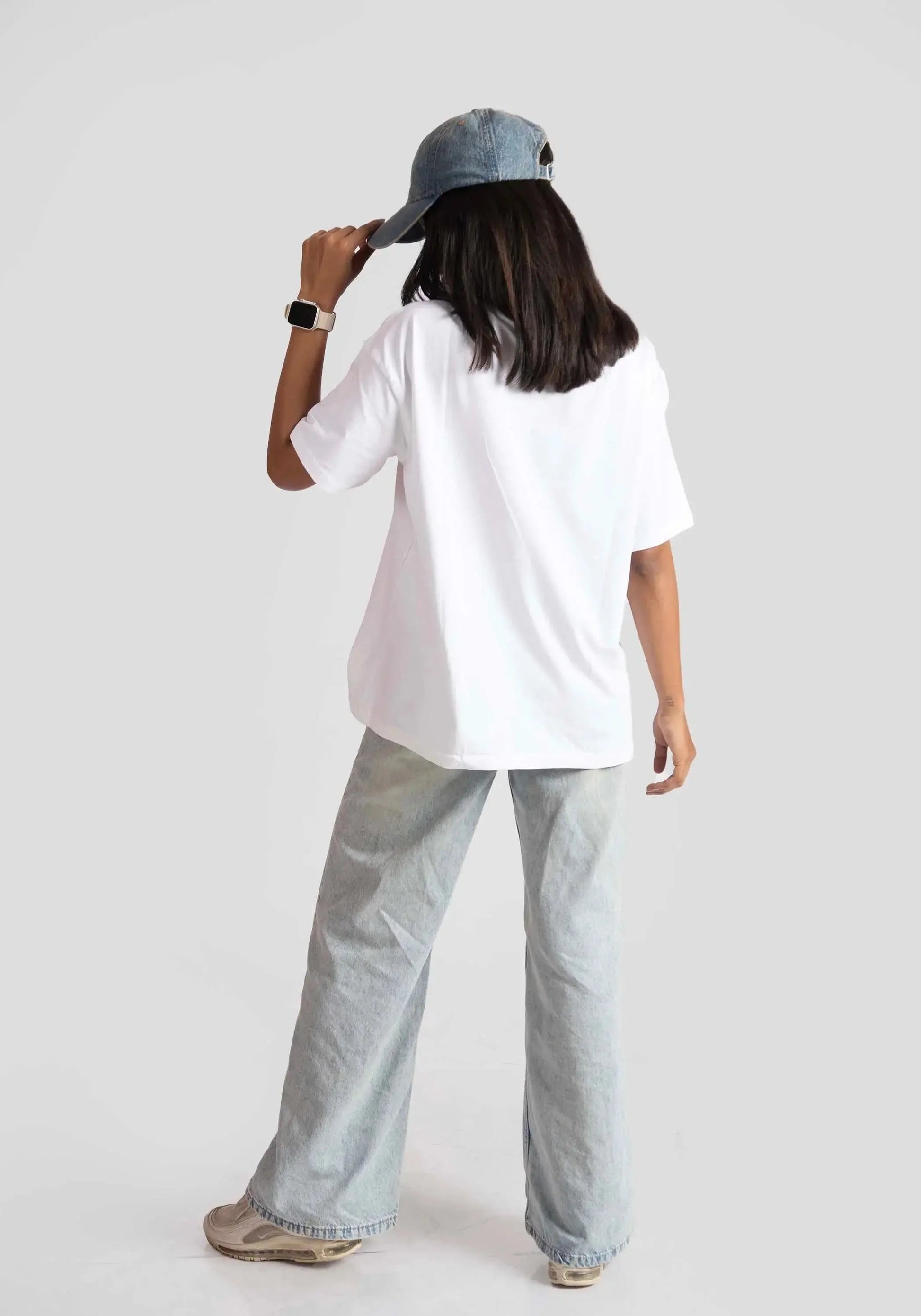 Back view of woman wearing white oversized anime t-shirt for women styled with wide-leg jeans and denim cap