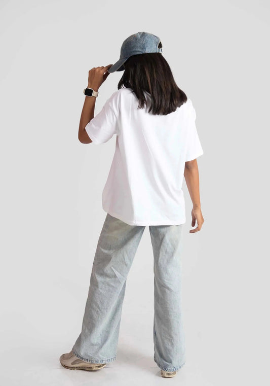 Back view of woman wearing white oversized anime t-shirt for women styled with wide-leg jeans and denim cap