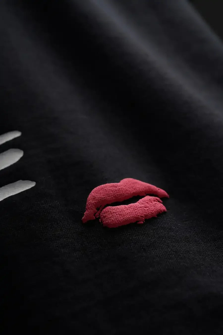 Black fabric with red embroidered lips and white embroidered lines on a dark background